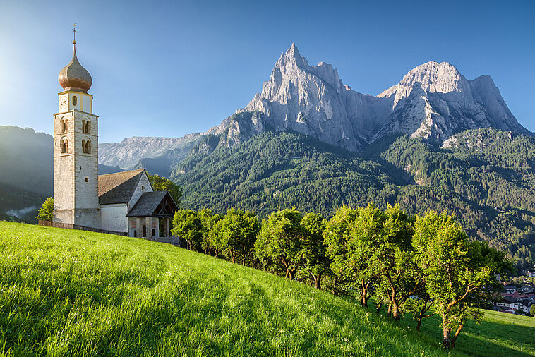 Blick auf eine Dorfkirche mit Dolomiten im Hintergrund