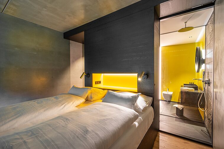 Blick in ein modernes Doppelzimmer mit Bad im Hintergrund