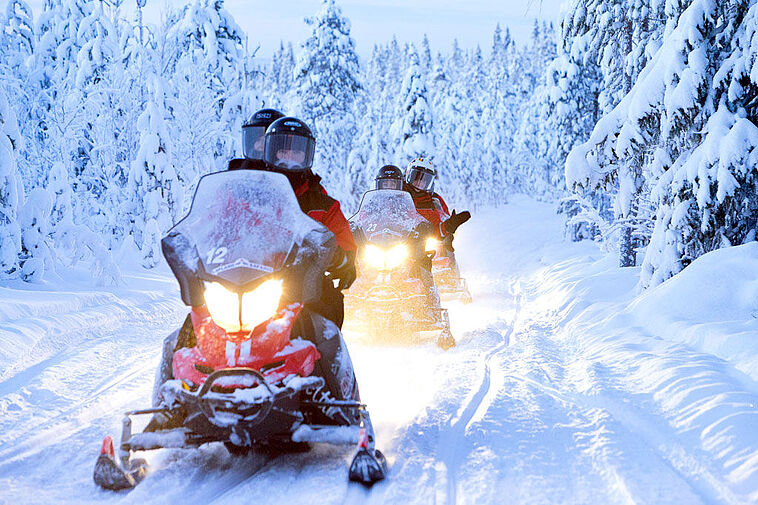 Mehrere Personen im Schnee auf Motorschlitten