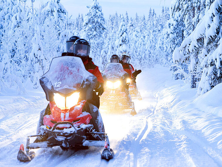Mehrere Personen im Schnee auf Motorschlitten