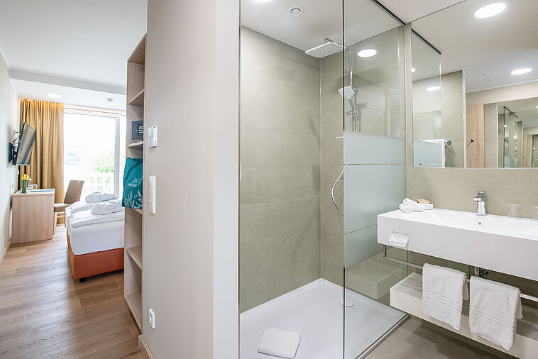 Blick vorbei an einem Badezimmer ins Doppelzimmer mit Balkon im Hintergrund
