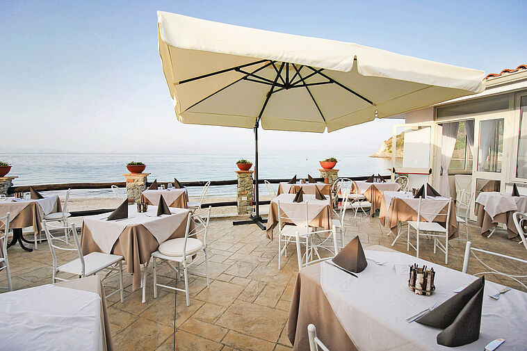 Blick über eine Terrasse mit einem Sonnenschirm und Meer im Hintergrund