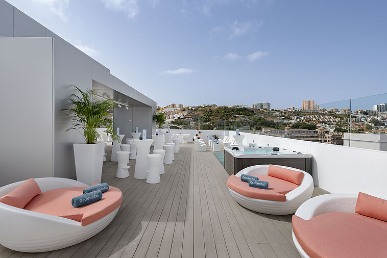 Blick über eine Dachterrasse mit weißen Möbeln und Stadt im Hintergrund